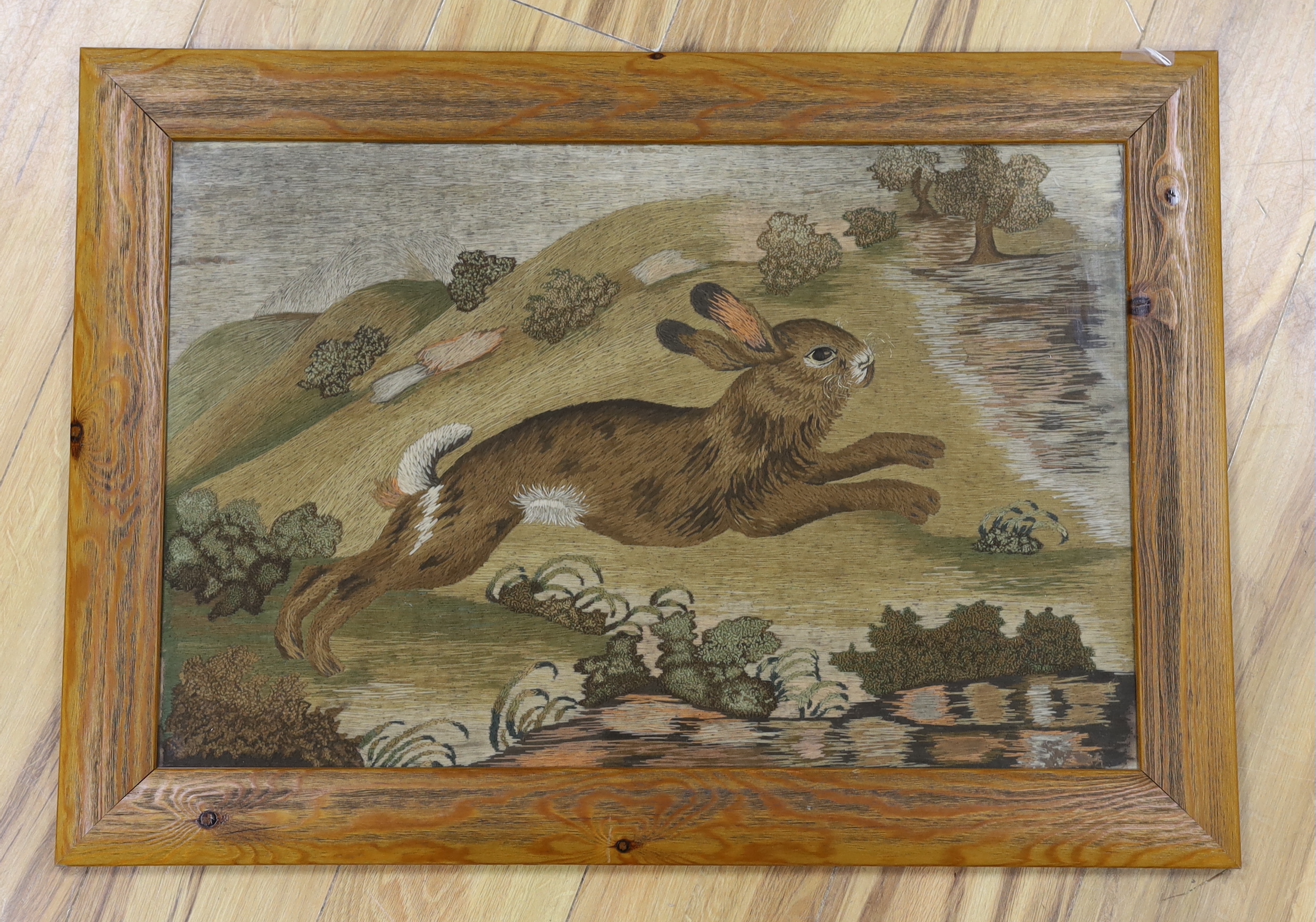 A late 19th century framed woolwork embroidered panel of a rabbit running through the countryside, worked mostly in stem stitch and raised knotting, 66.5cm wide x 42cm high